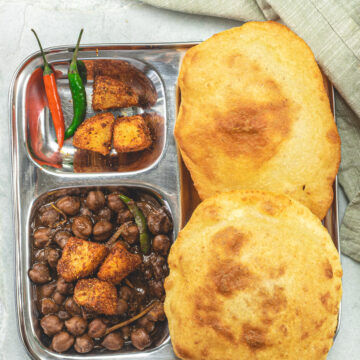 A plate of chole bhature with green chilies on the side.