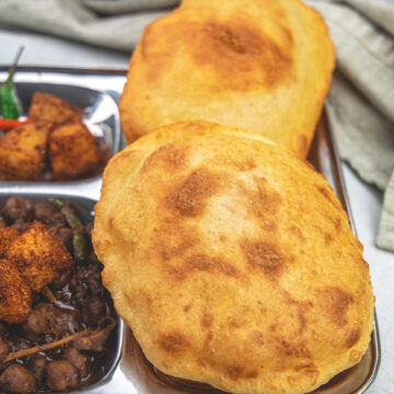 2 bhature in a plate with bhole and khatte aloo.