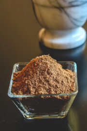 Garam masala powder in a bowl with marble mortar in the back.