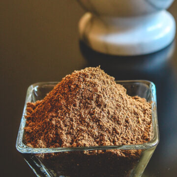 Garam masala powder in a bowl with marble mortar in the back.