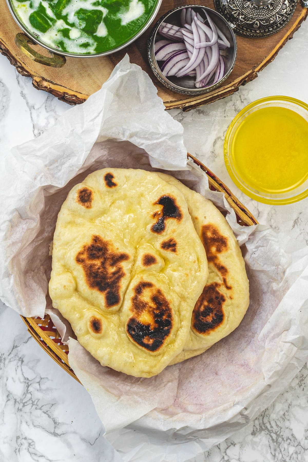 Naan bread in a parchment-lined basket with palak paneer, onion and ghee on the side.