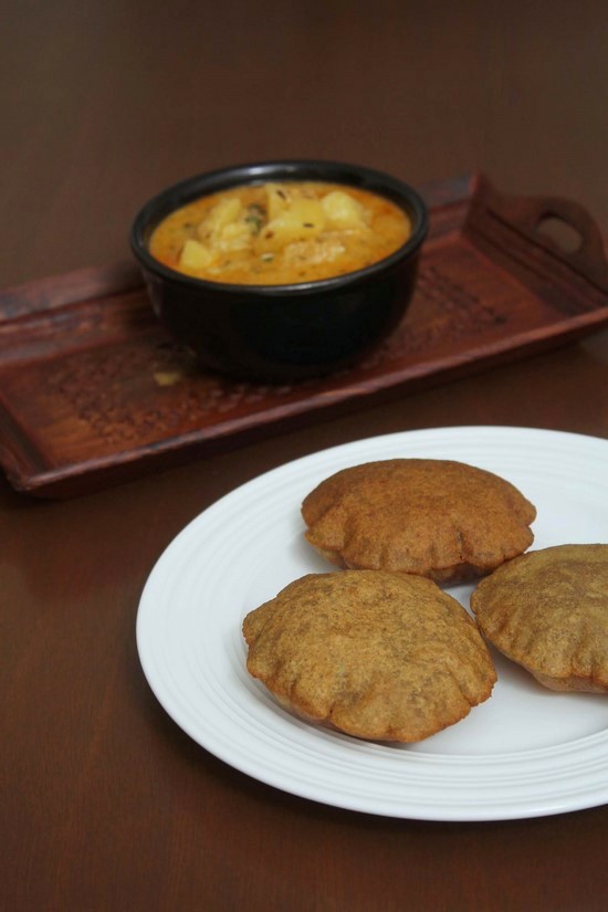 Singhare ki puri in a plate with a bowl of dahi aloo in the back.