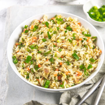 A bowl of veg fried rice with napkin, forks on the side.