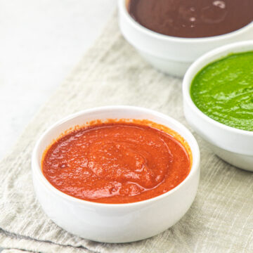 Garlic chutney bowl with green chutney and meethi chutney bowls in the back.