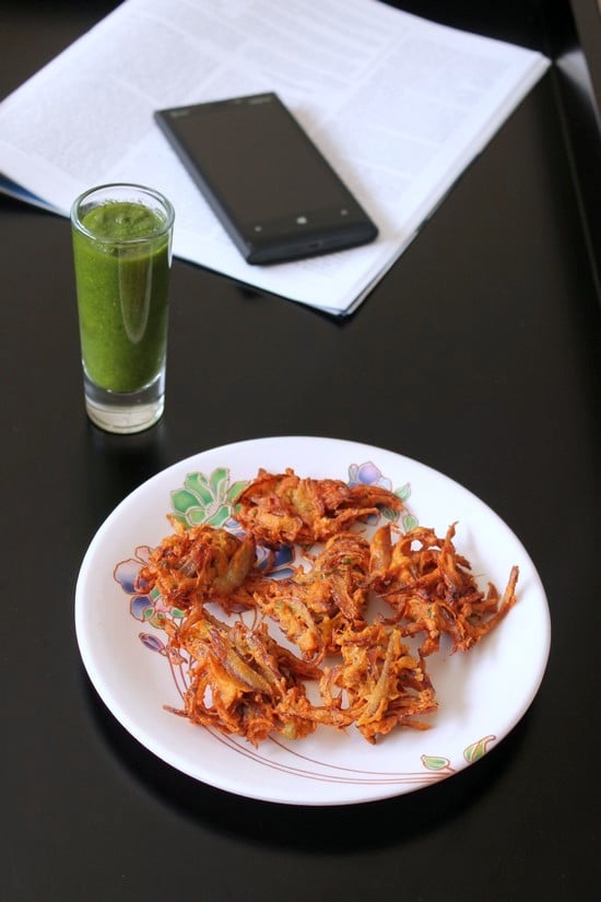 Onion Pakoda with green chutney and magazine and phone in the back.