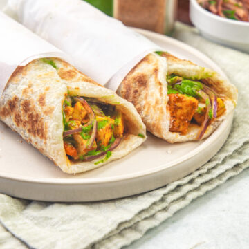2 paneer kathi roll in a plate with napkin under it.