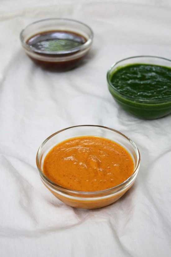 Red Garlic Chutney in a bowl with meethi chutney and green chutney bowls in the back.