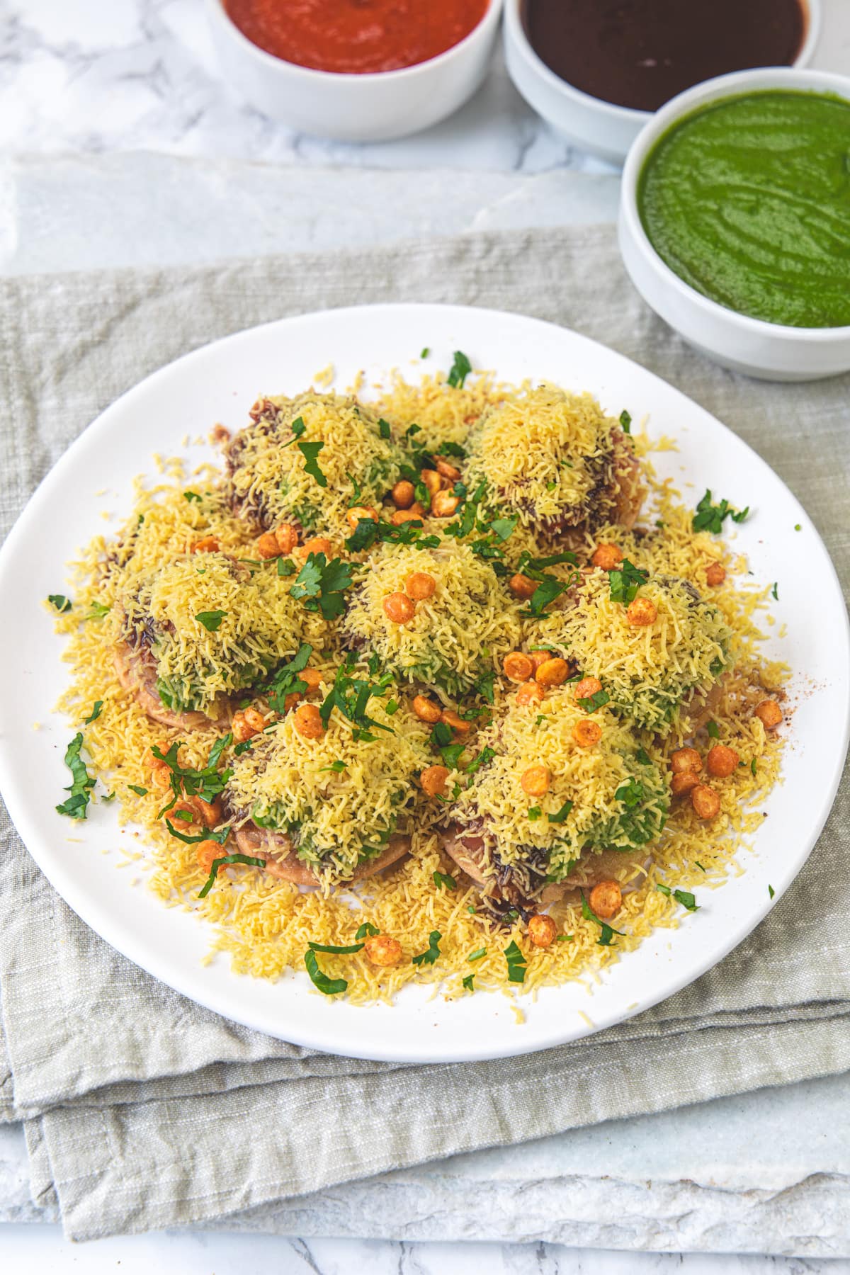 A plate of sev puri chaat under the napkin with 3 chutney bowls.