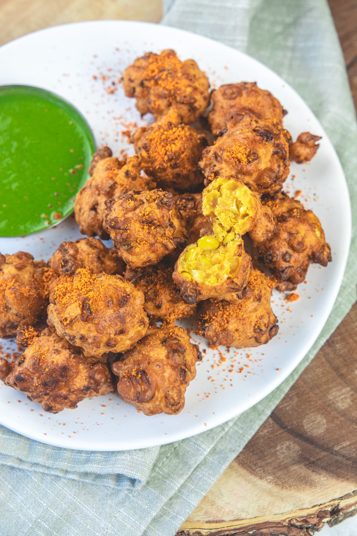 A plate of corn pakora and one is cut open, served with green chutney.