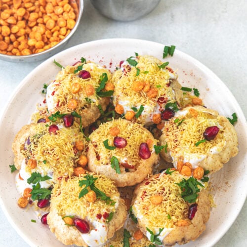 A plate of dahi batata puri with a bowl of chana dal and green chutney in the back.