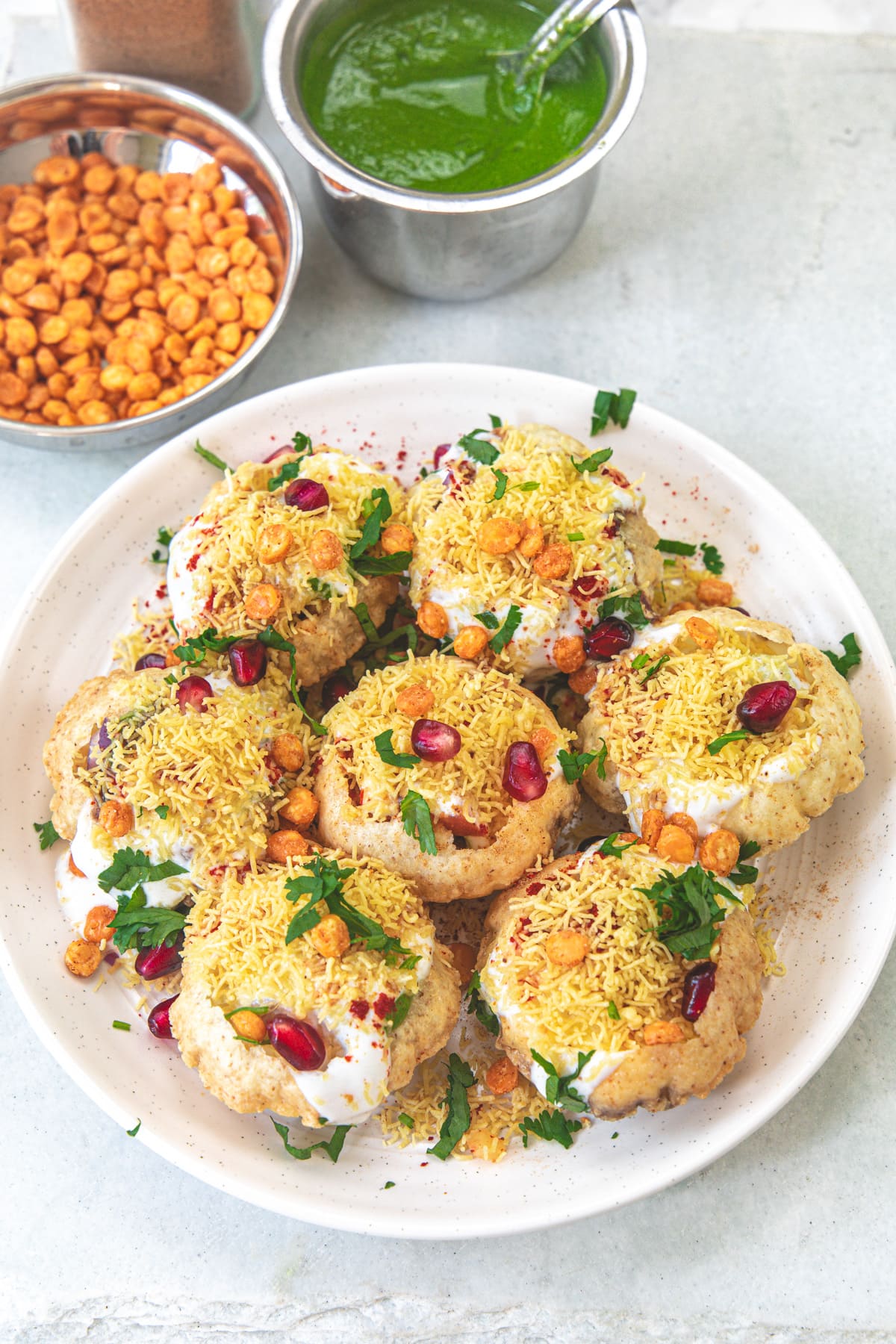 A plate of dahi batata puri with a bowl of chana dal and green chutney in the back.