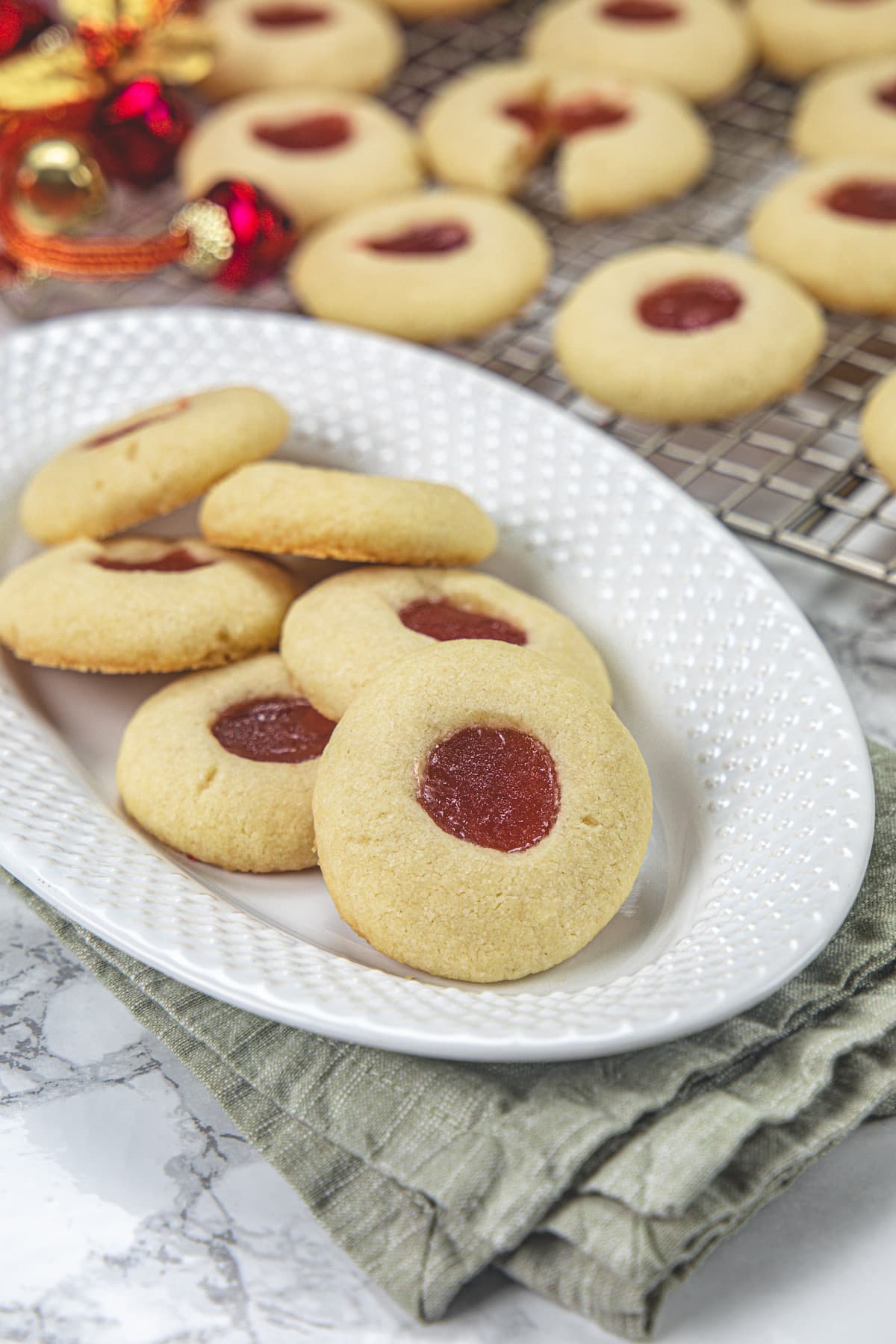 Shortbread thumbprint cookies in a plate and a few more in the back on a cooling rack.