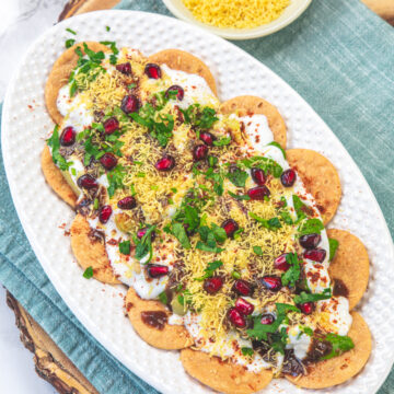 A plate of papdi chaat with napkin under the plate and a bowl of sev on the side.