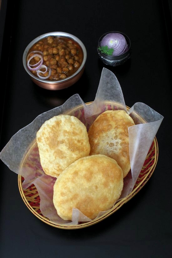 Instant bhatura in basket with chole and onion in the back.