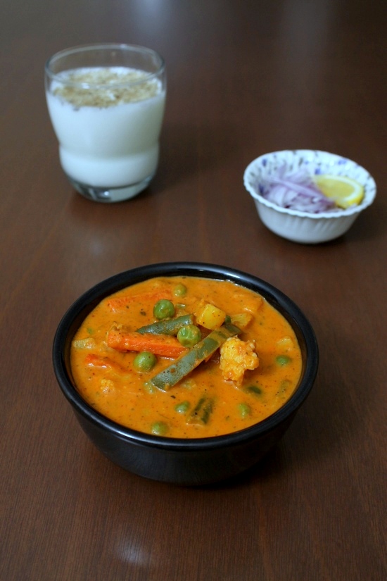 Veg Makhanwala served in a bowl with a glass of chaas and sliced onion in the back.