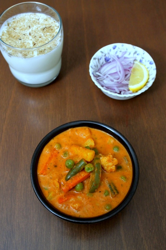 Veg Makhanwala served in a bowl with sliced onions and lemon wedges and chaas in the back.