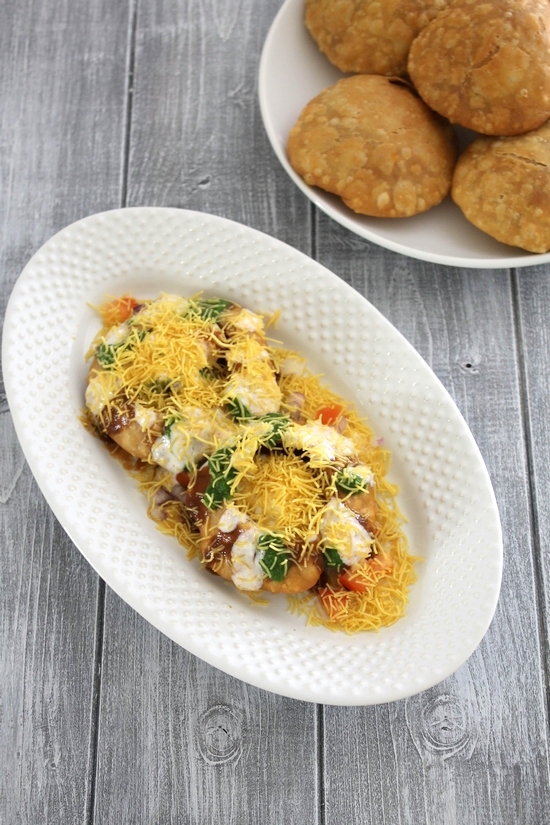 khasta kachori chaat in an oval plate with a few more kachori in a plate in the back.