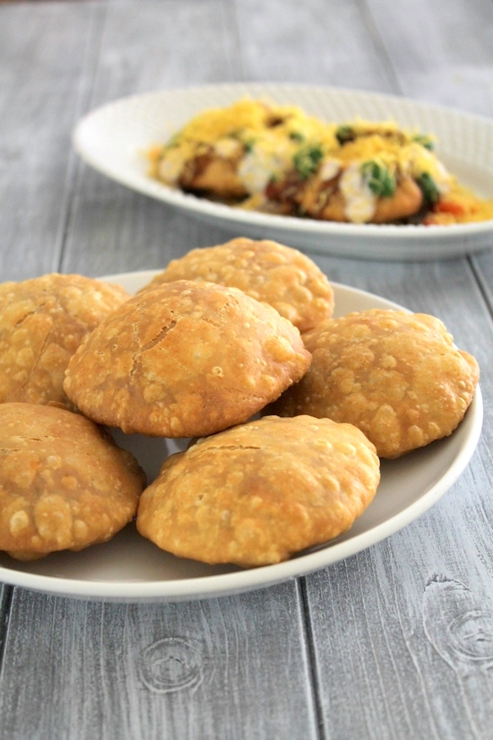 A stack of kachoris in a plate with kachori chaat plate in the back.