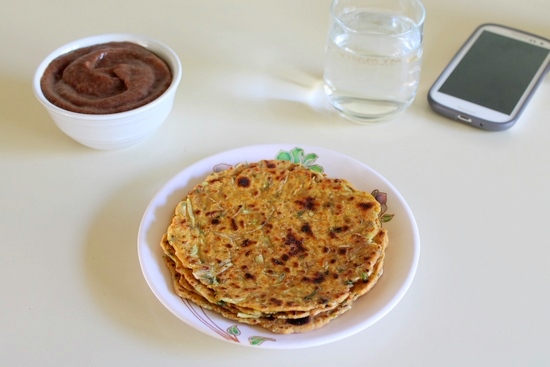 Lauki Thepla in a plate with chutney and a glass of water and phone in the back.