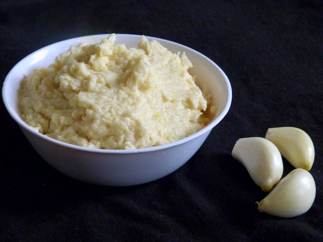 Garlic paste in a bowl with 3 cloves of garlic on the side.