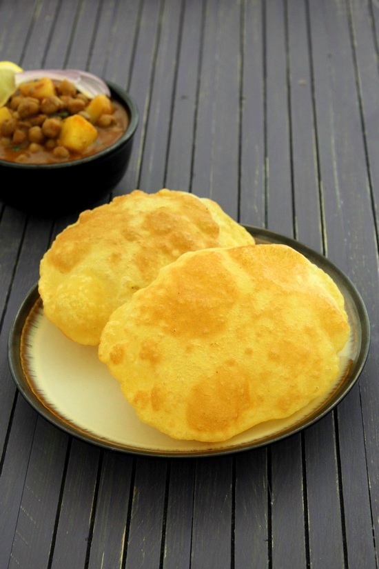Aloo bhatura in a plate with chole in the back.