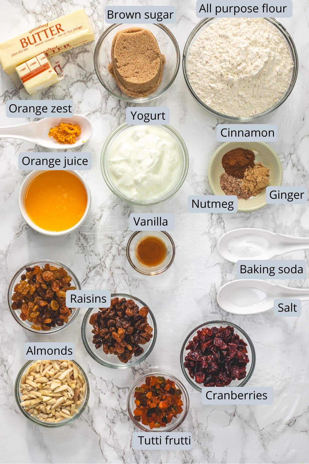 Eggless fruit cake ingredients in bowls and spoons with labels.