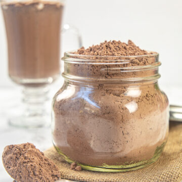 Hot cocoa mix in a jar with a spoon full on the side.