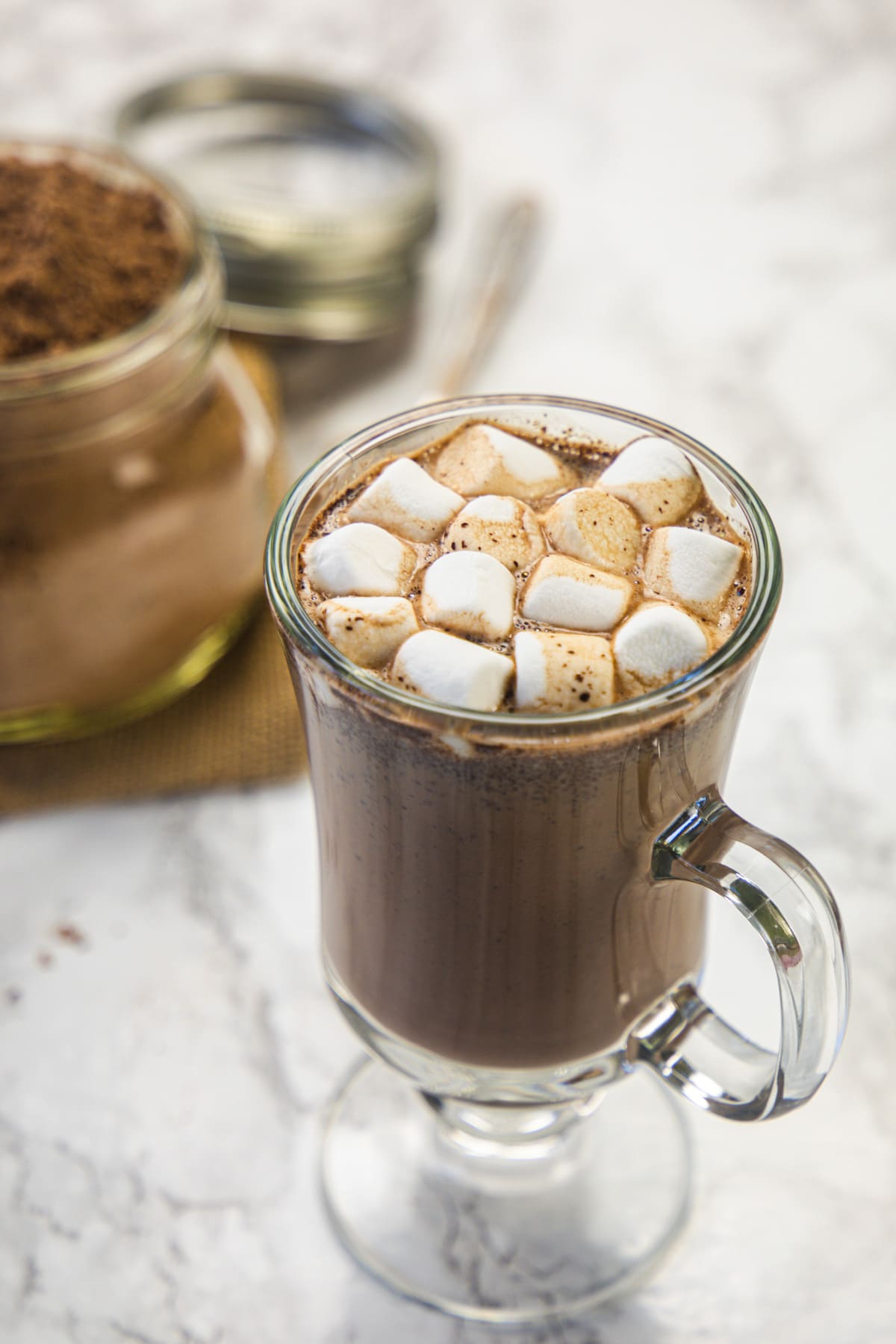 Hot chocolate drink topped with marshmallows and hot chocolate mix in the back.
