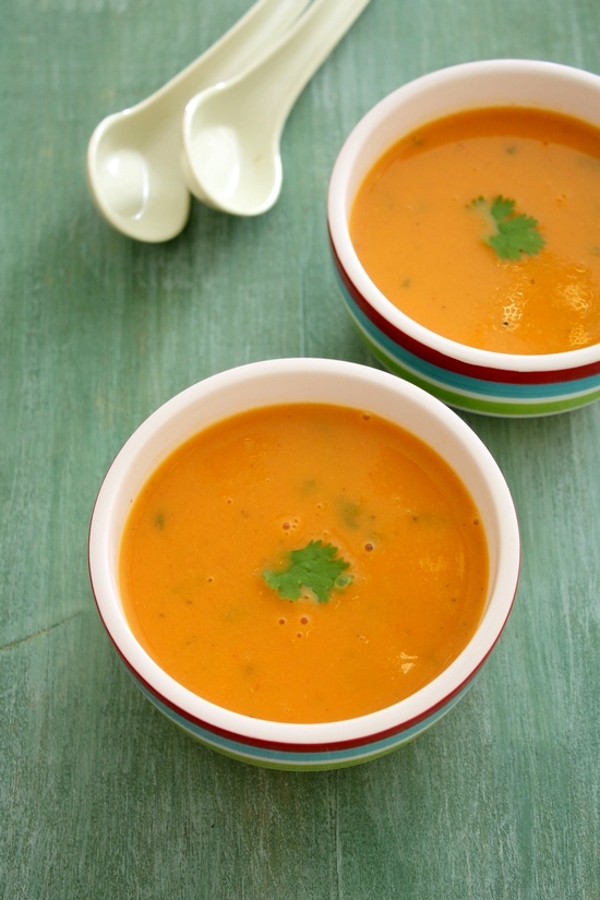 2 bowls of tomato shorba garnished with cilantro with 2 spoons on the side.