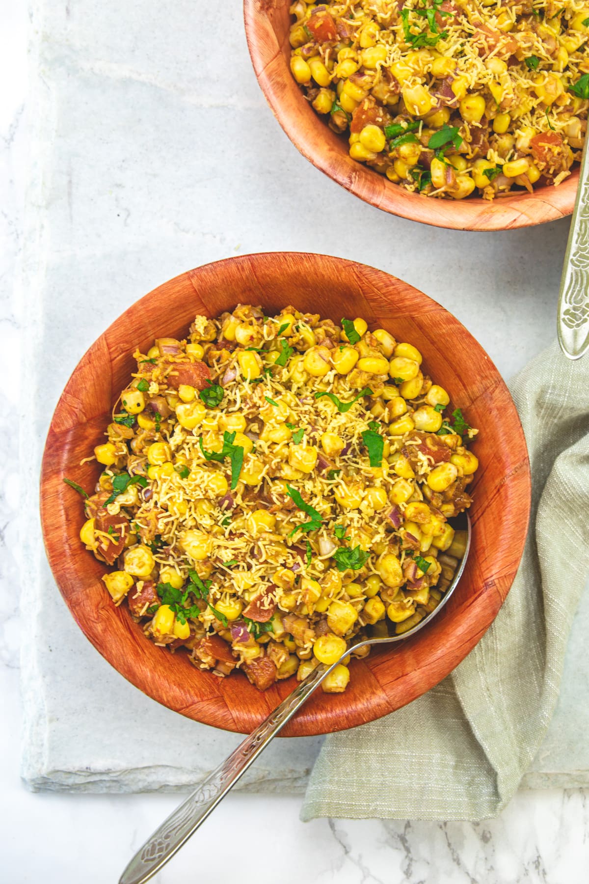 2 bowls of corn bhel with spoon and napkin on the side.