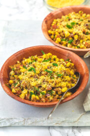 Corn chaat in 2 bowls with spoons on a marble board.