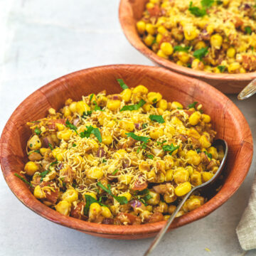 Corn chaat in 2 bowls with spoons on a marble board.