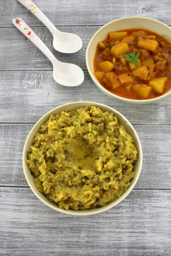 Gujarati khichdi in a plate with ghee and a plate of shaak in the back with spoons on the side.