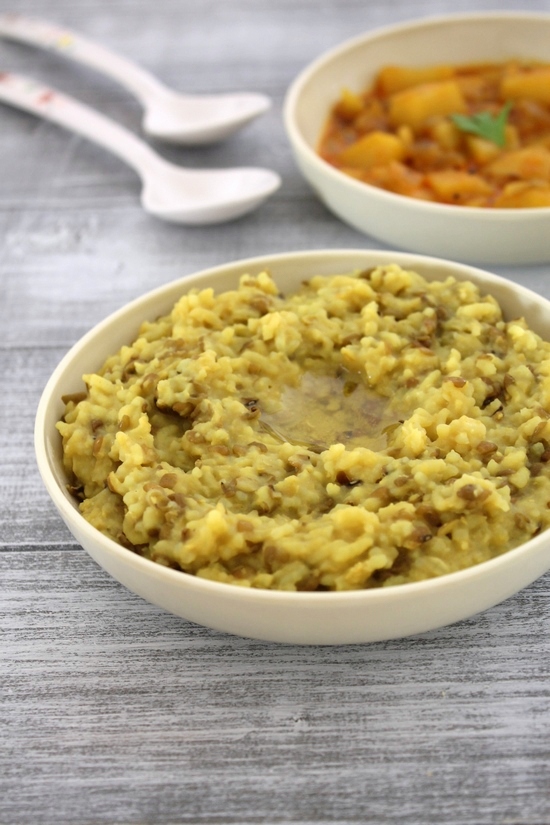 Gujarati khichdi with a drizzle of ghee with sabzi and spoons in the back.