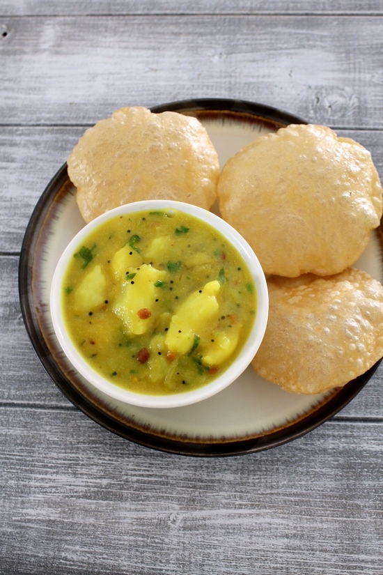 Potato masala served in a bowl and 3 poori in the plate.