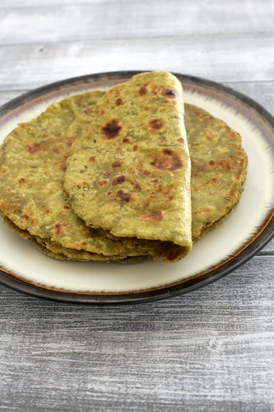 A stack of aloo palak paratha in a plate with first paratha folded in half.