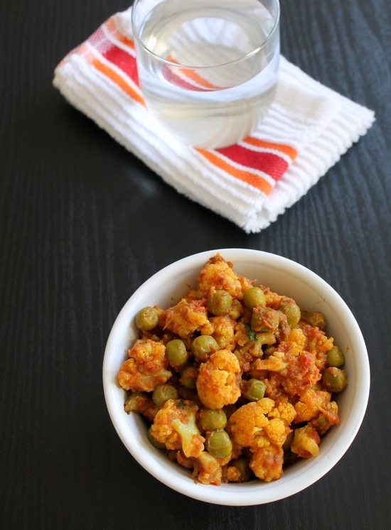 Gobi matar in a bowl with a glass of water in the back.