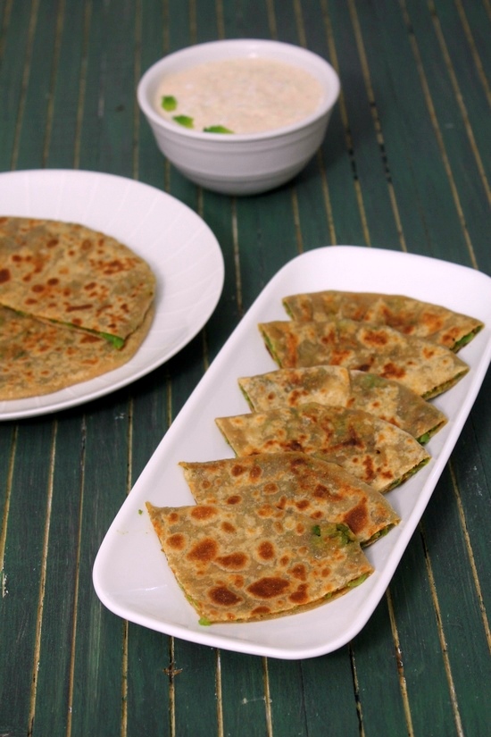 Matar paratha triangles in a plate with yogurt in the back.