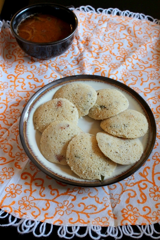 7 oats idli in a plate and a bowl of sambar in the back.