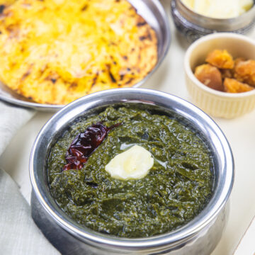 Sarson ka saag topped with butter and served with sides.