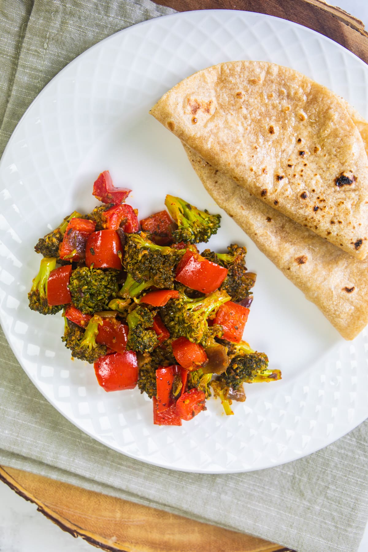 Broccoli sabzi served in a plate with 2 rotis in a white plate.