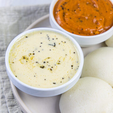 Coconut chutney bowl with a side of idli and tomato chutney bowl.