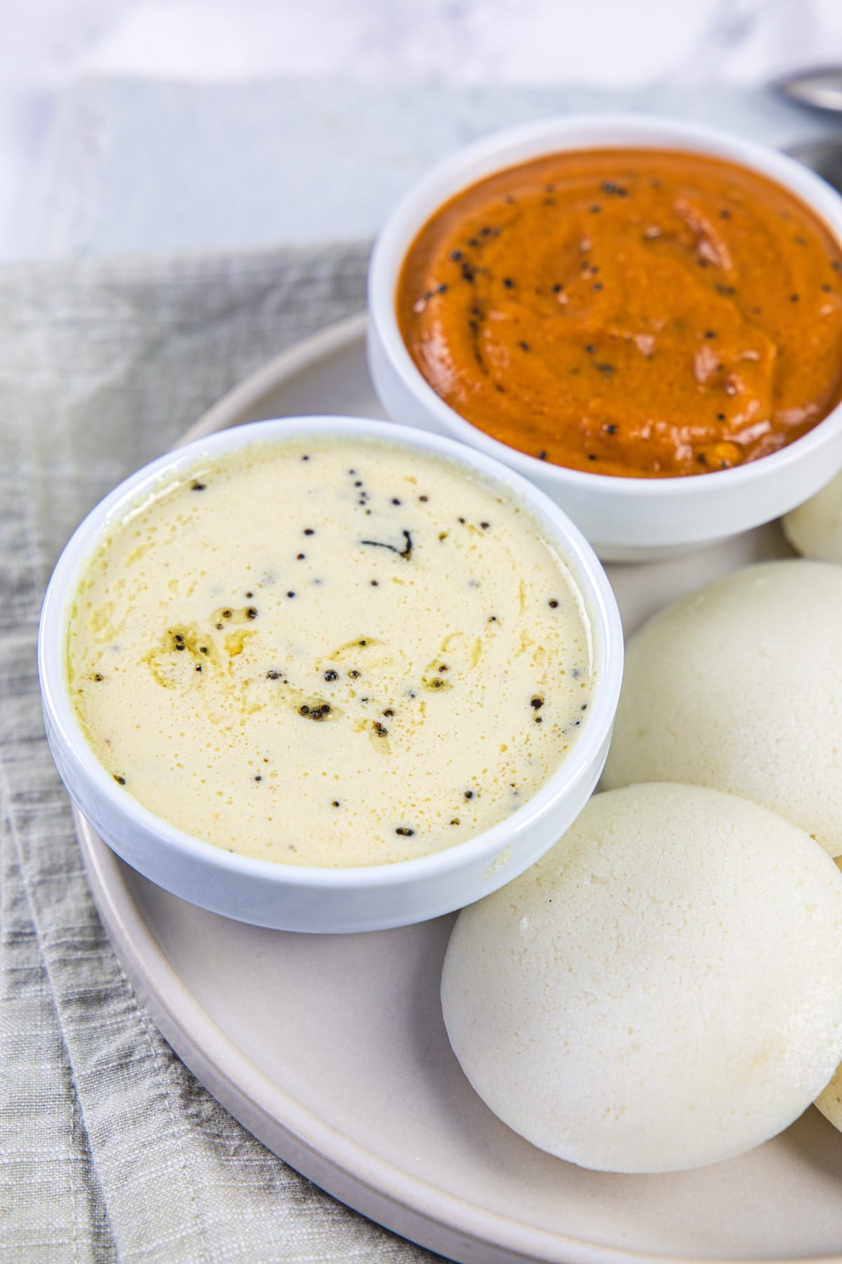 Coconut chutney bowl with a side of idli and tomato chutney bowl.