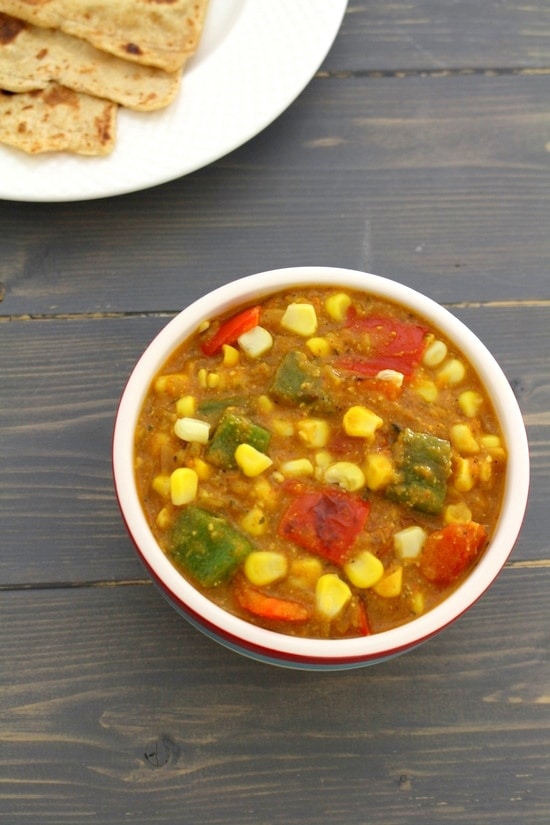 Corn capsicum masala in a bowl with paratha in the back.