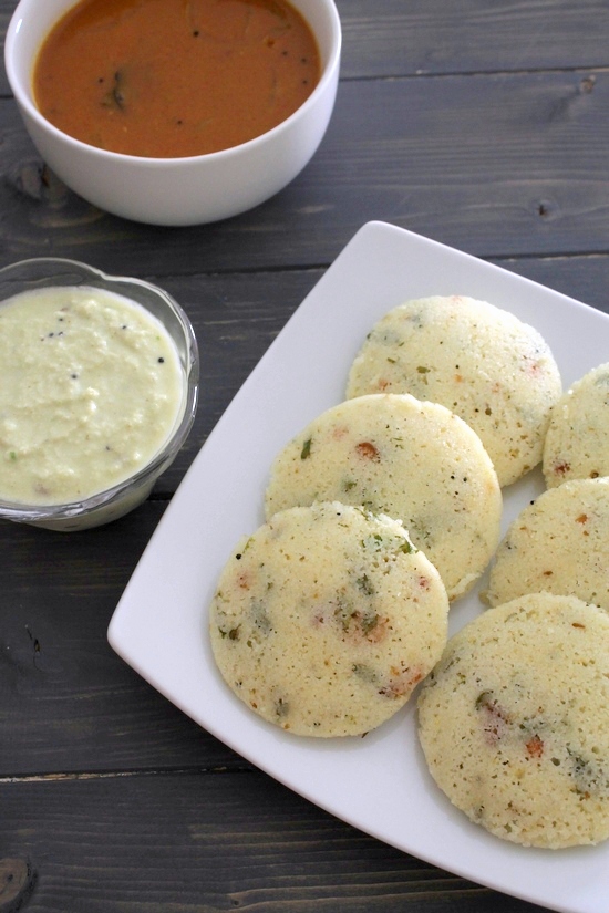 Rava idli served in a plate with sambar and chutney bowls on the side.