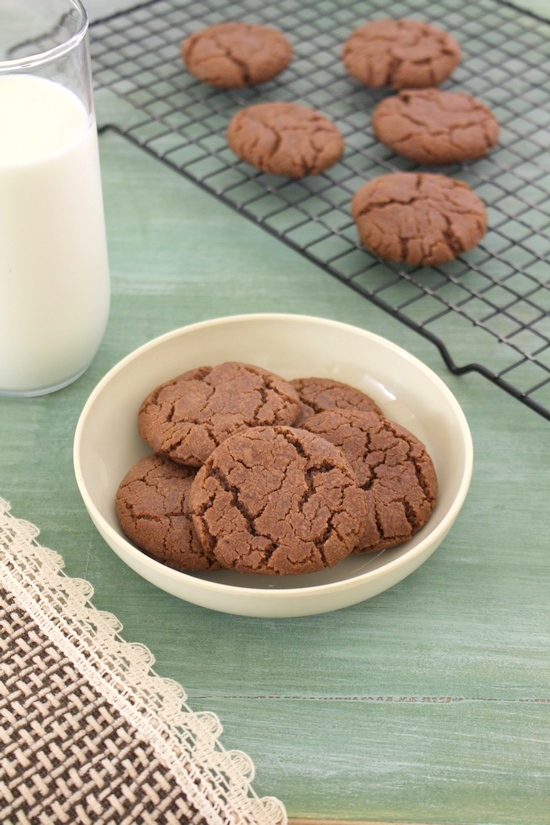 Eggless nutella cookies in a plate with a glass of milk and more cookies in the back.