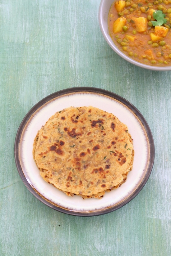 Onion paratha served with aloo matar in the back.