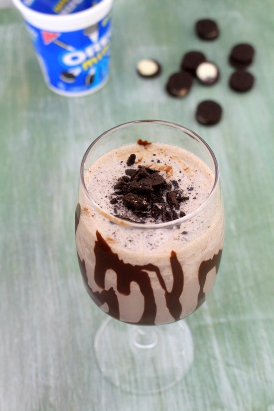 Oreo milkshake in a glass topped with crushed oreos and more oreo cookies and packet in the back.