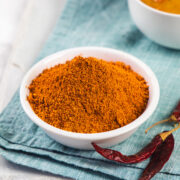Sambar powder in a bowl with dried chilies and sambar bowl on the side and napkin under it.