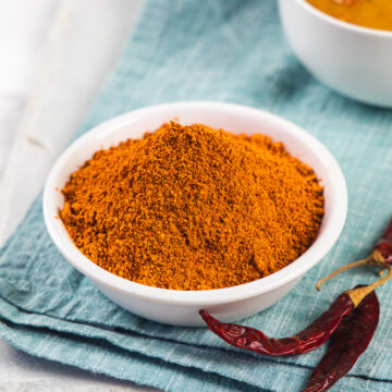 Sambar powder in a bowl with dried chilies and sambar bowl on the side and napkin under it.